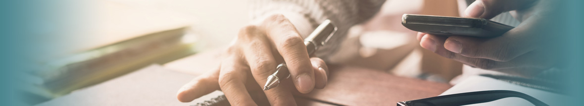 person using a phone while taking notes, closeup of hands